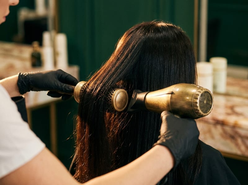 Hands shaping hair with a round brush.